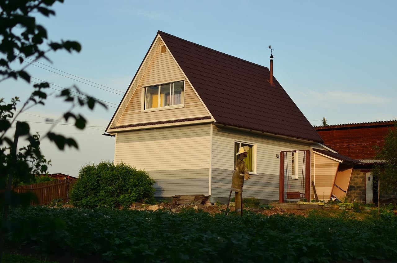 About A suburban house with garden and scarecrow under warm evening sunlight, showcasing rustic charm.