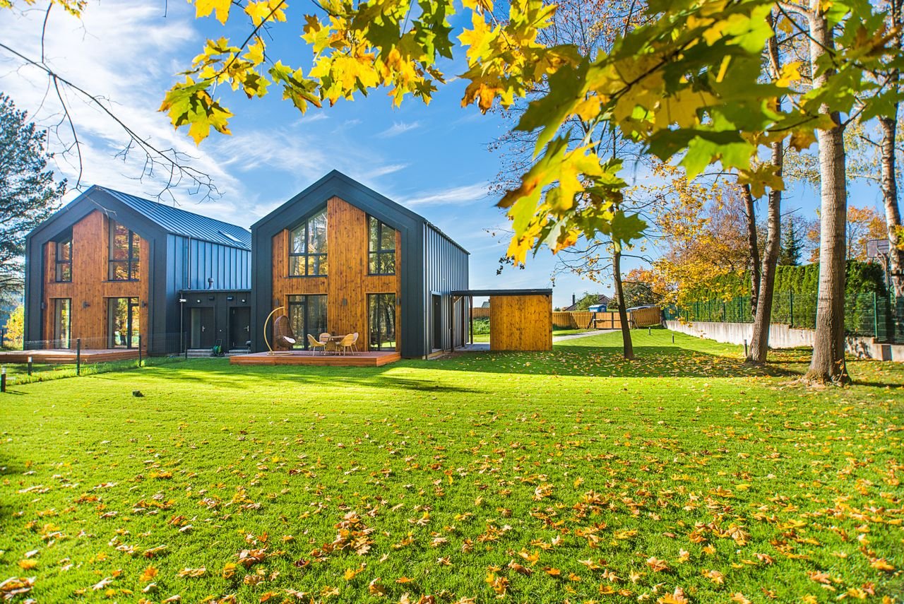 Services Contemporary wooden houses with lush green lawns surrounded by vibrant autumn foliage.