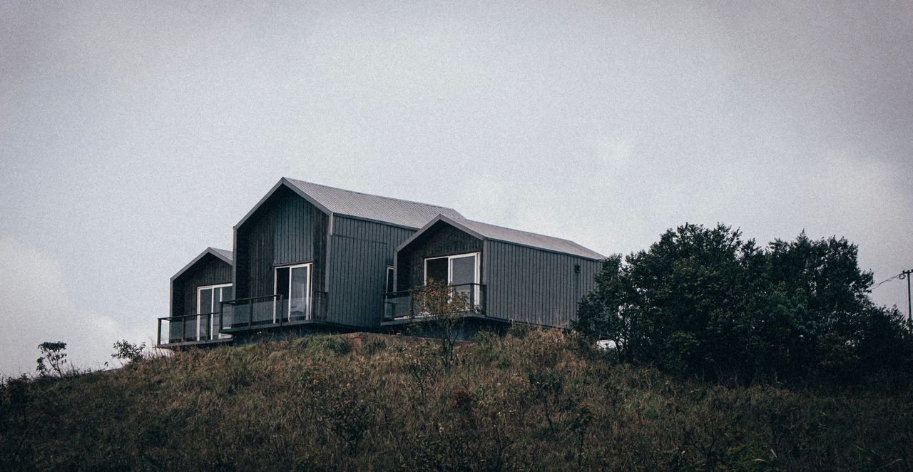 Services Contemporary cabin perched on a hillside in a cloudy, rural setting.