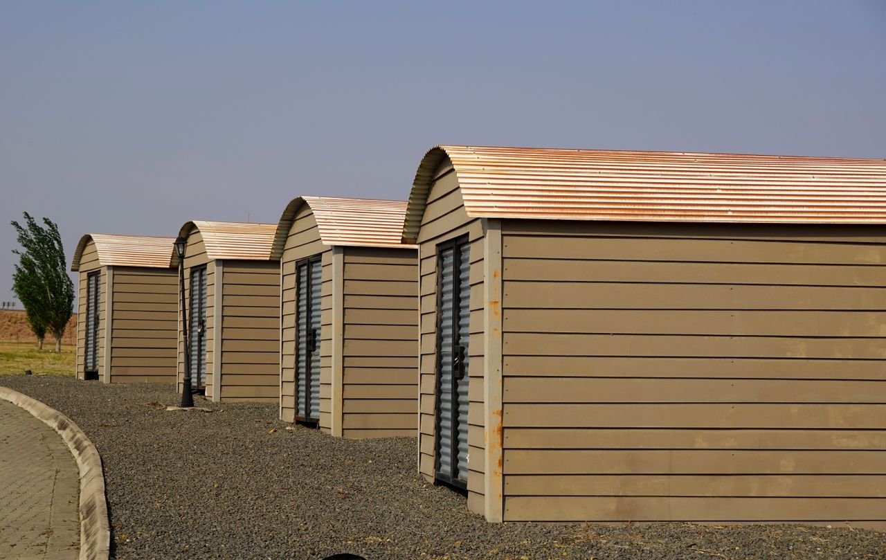 Services Four identical modern storage sheds aligned on a gravel surface with clear skies.
