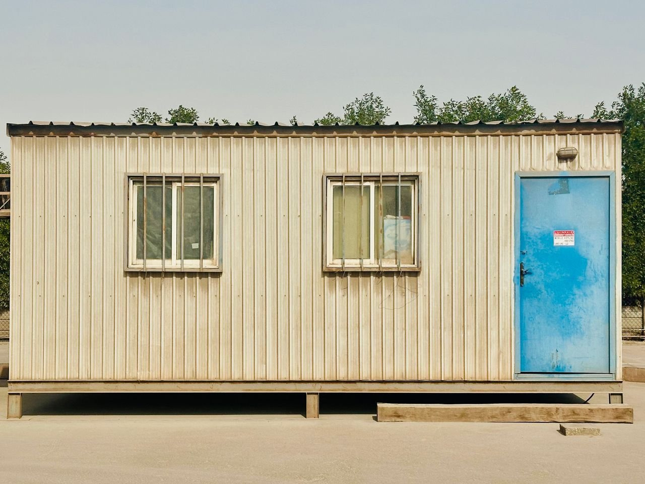 Services A portable cabin with a distinctive blue door in a sunny outdoor setting in Saudi Arabia.