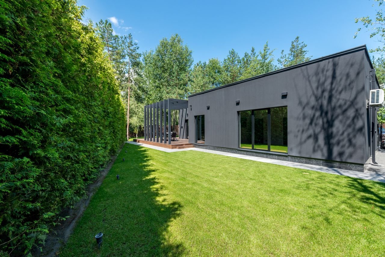 Services Sleek black modern house with large windows and vibrant green lawn surrounded by dense trees.