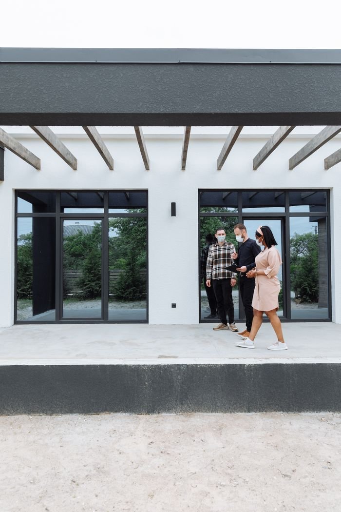 Services Three real estate agents wearing masks showcase a sleek, modern home exterior to clients.